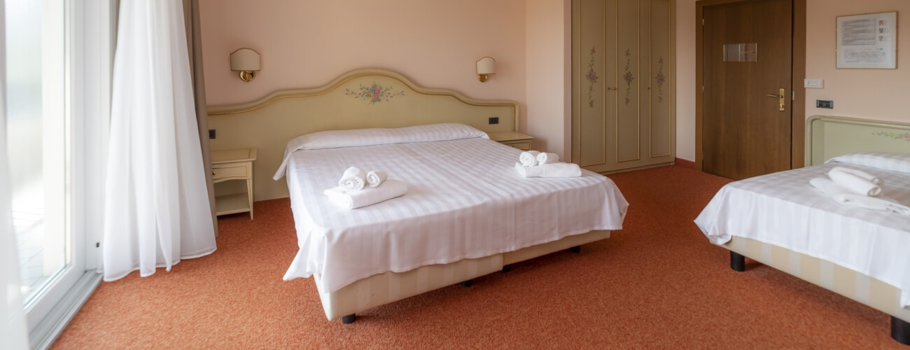 Camera d'hotel con un letto matrimoniale e un letto singolo, pareti pesca, tappeto arancione e armadio con design floreale.