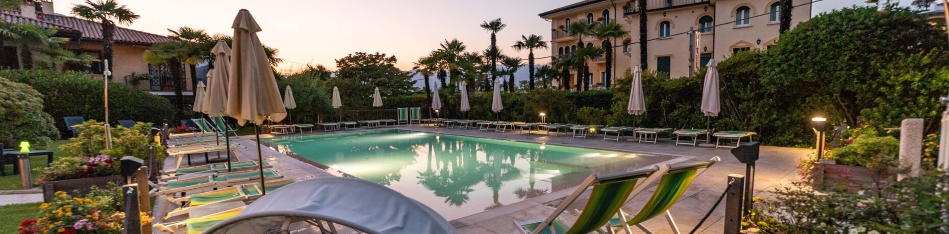 Serene outdoor pool scene with lush greenery, lounge chairs, and a multi-story building under a soft pink sky.