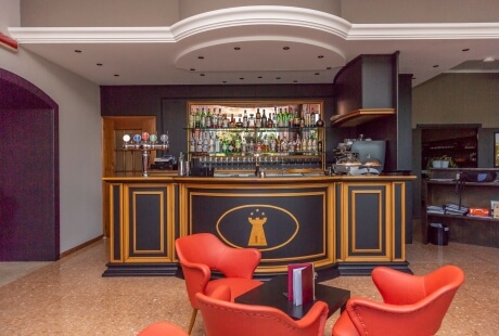 A stylish bar area featuring a black counter with gold trim, beer taps, red chairs, and a variety of beverages on display.