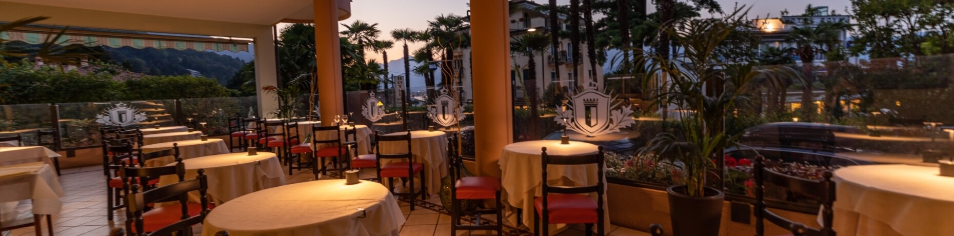 Serene outdoor dining area at dusk with elegant tables, potted plants, and warm orange glow, creating a tranquil ambiance.