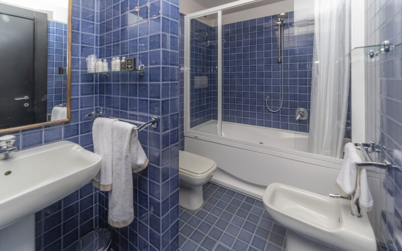 Modern bathroom with blue tiled walls, white fixtures, a bathtub with glass doors, and a clean, well-maintained appearance.