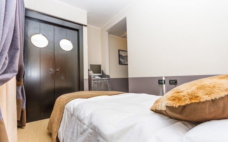 Camera da letto accogliente con letto, armadio marrone e scrivania, pareti bianche e taupe, e tappeto beige.