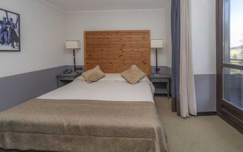 Cozy hotel room with a double bed, nightstands, lamps, a window, and decorative picture on the wall.