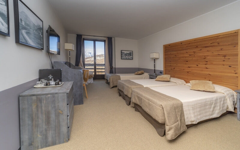 Camera d'hotel con due letti, vista montana, mobili in legno e decorazioni in bianco e grigio. Atmosfera pulita e accogliente.