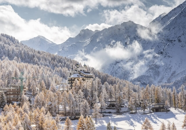 Winter landscape in a valley with snow-covered mountains, a picturesque village, and a blue sky with fluffy clouds.