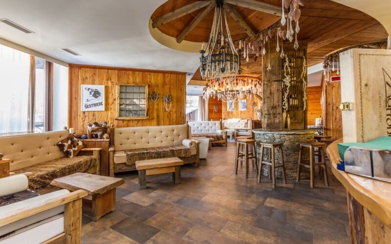 Interno di un ristorante rustico e accogliente con pareti in legno, chandelier, finestre luminose e comodi posti a sedere.