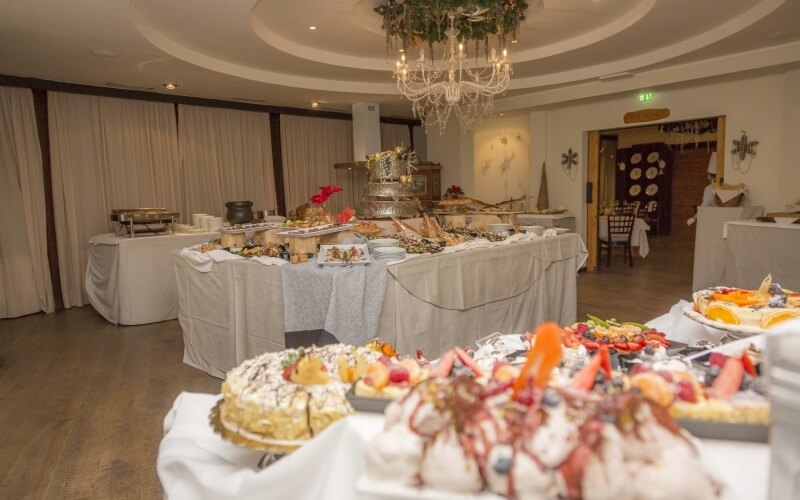 Sala da pranzo a buffet decorata per un evento, con dolci, tavoli imbanditi e un grande lampadario.