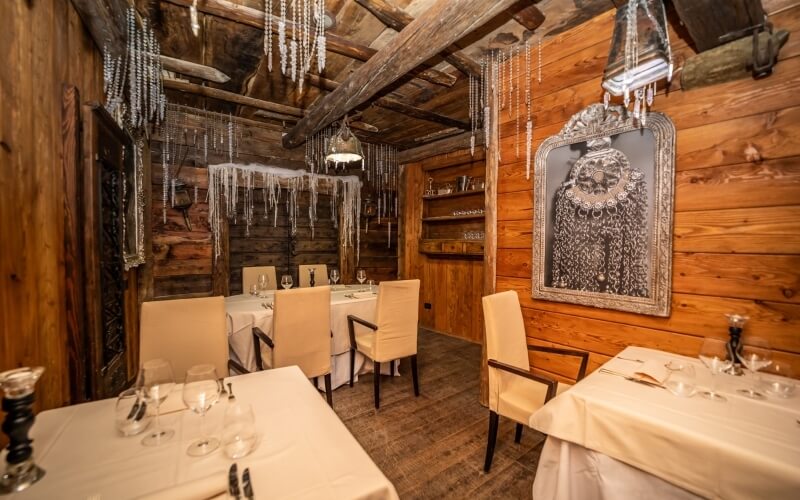 Dimly lit dining room with wooden walls, elegant tables, chandeliers, and a large ornate mirror, exuding warmth and sophistication.