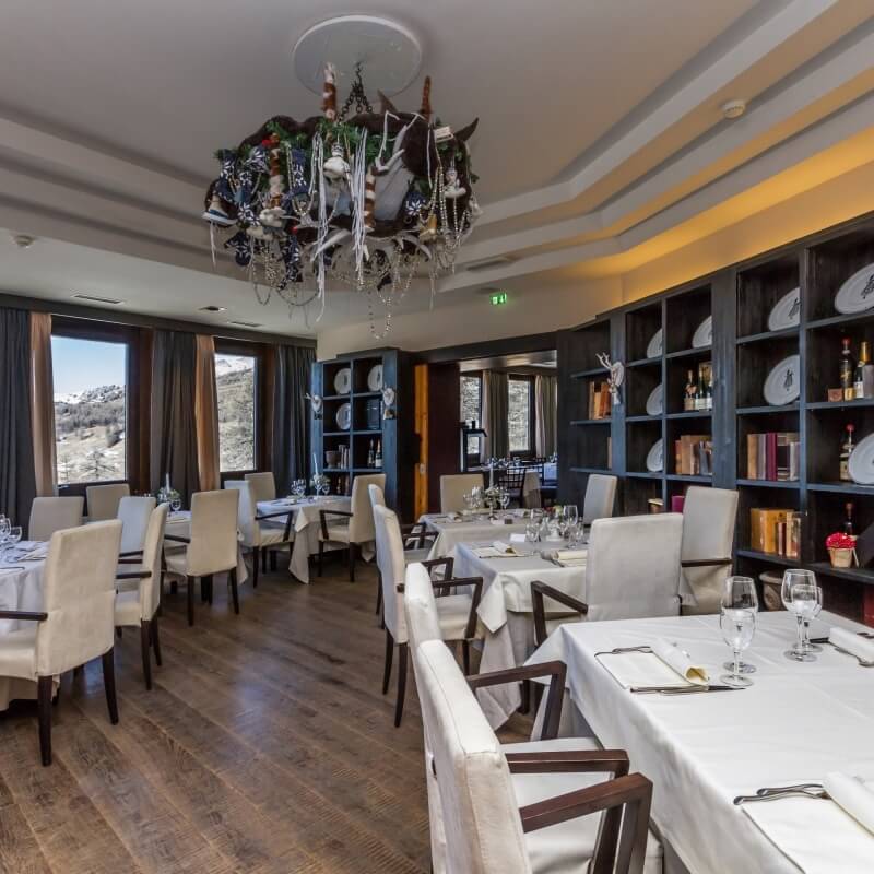 Formal dining room with dark wood floor, white walls, tables set for dinner, chandelier, and mountain view window.