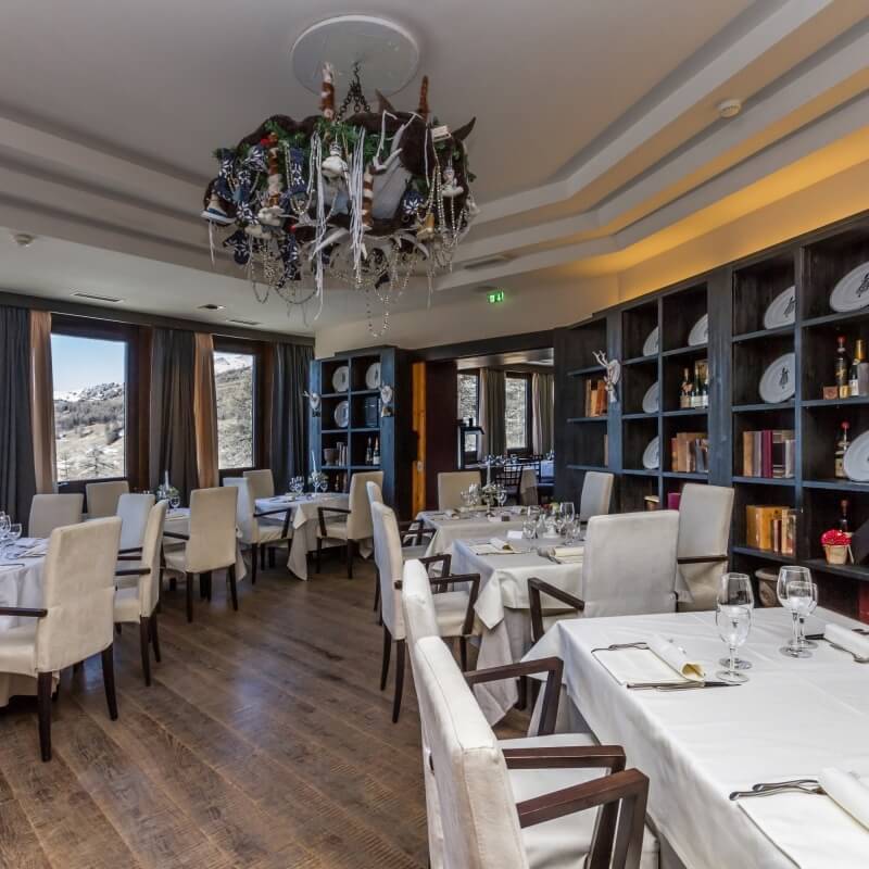 Formal dining room with dark wood floor, white walls, tables set for dinner, chandelier, and mountain view window.