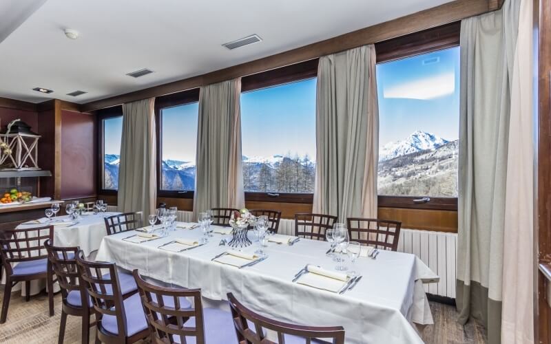 Sala da pranzo elegante con tavolo imbandito, vista sulle montagne innevate e atmosfera accogliente.