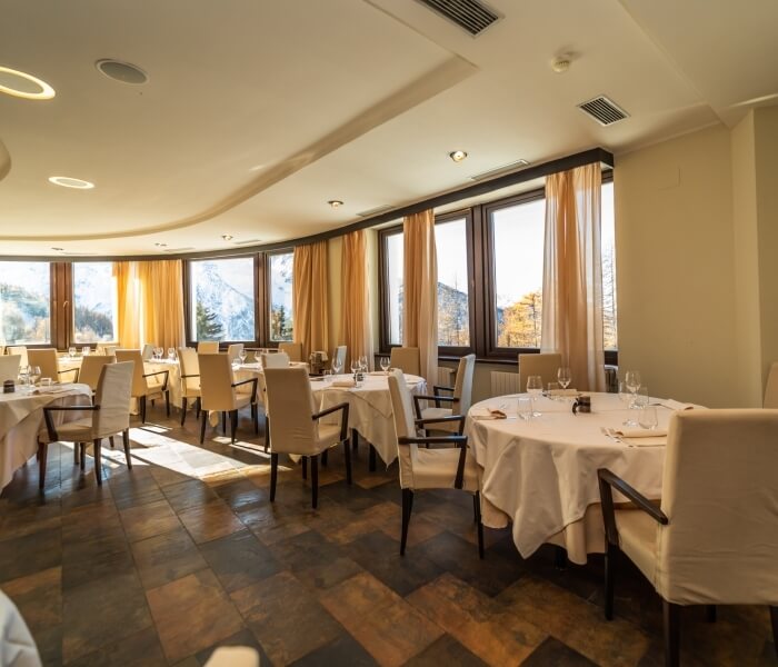 Elegant dining room with curved wall, round tables set with white tablecloths, and large windows with sheer curtains.