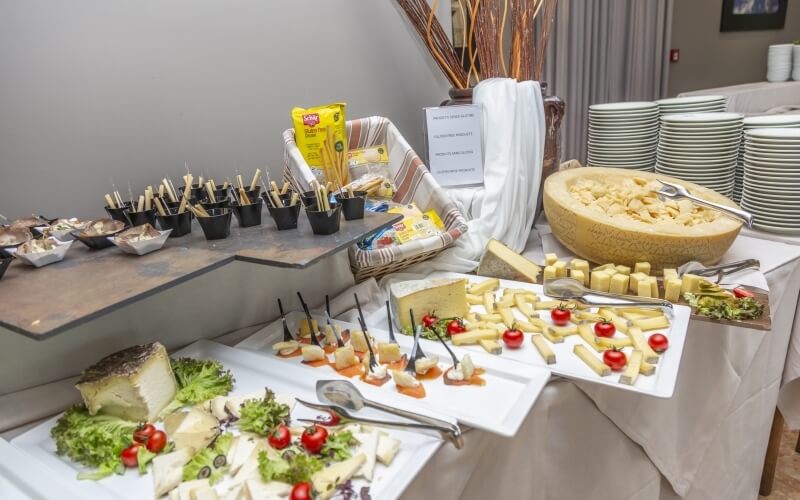 A beautifully arranged table with assorted cheeses, condiments, and breadsticks on a white tablecloth, set against gray curtains.