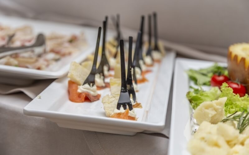 Close-up of a table setting with cream cheese and salmon, shrimp, a bundt cake, and assorted finger foods for a buffet.