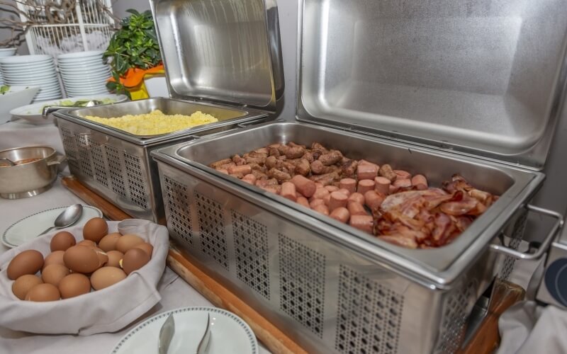 Buffet setup with mashed potatoes, assorted meats, brown eggs, plates, bowls, and a decorative birdcage in the background.