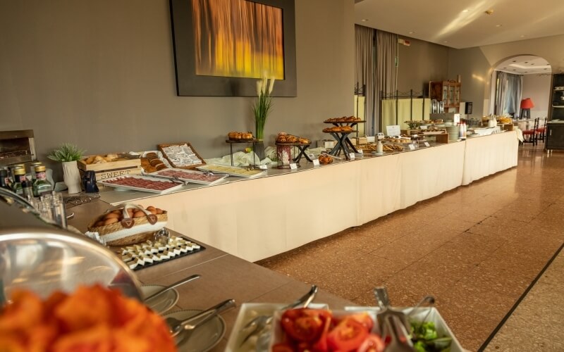 A buffet table with assorted dishes in a spacious room featuring gray walls, high ceilings, and decorative elements.