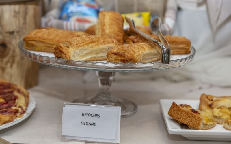 A buffet table featuring a glass cake stand with golden-brown puff pastries and a silver serving utensil on top.