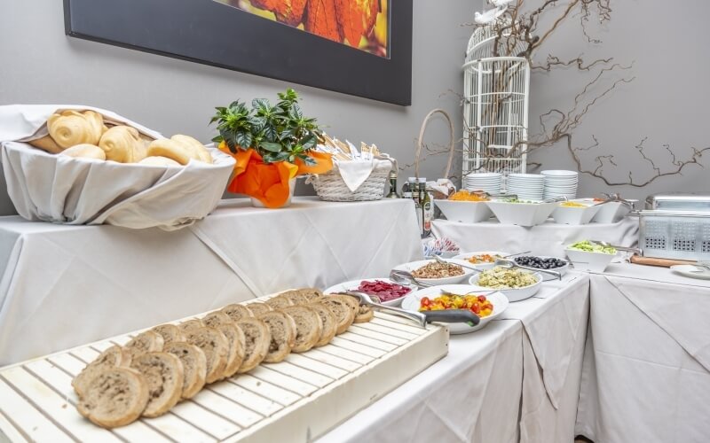 Buffet table with assorted food, including bread and pastries, white decor, and a vibrant framed image above.