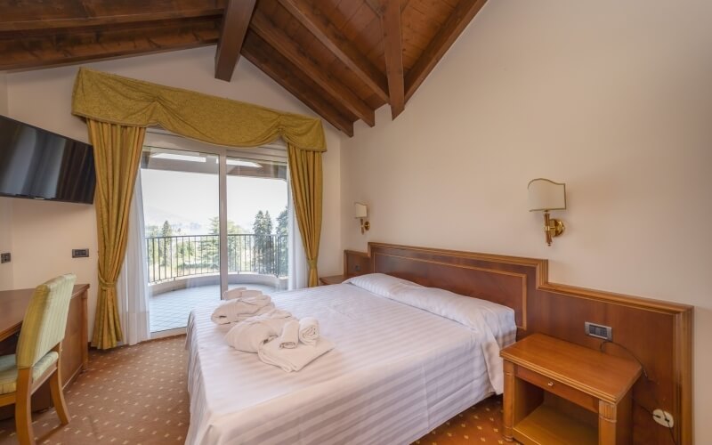 Serene hotel room with a double bed, desk, and balcony view, featuring wooden beams and a warm, inviting ambiance.