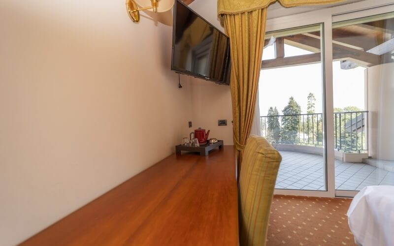 A bright room with a large window, sliding glass doors to a balcony, wooden table, yellow chair, and mounted TV.