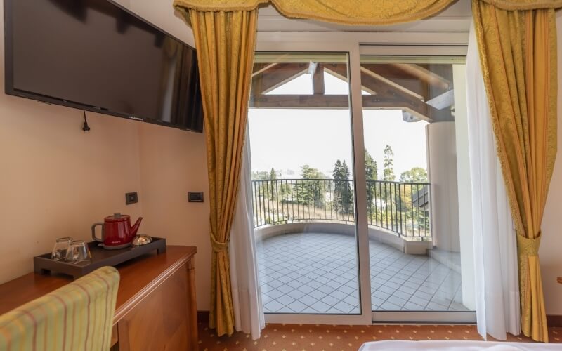 Cozy hotel room with balcony, TV, dresser, kettle, and striped chair, featuring yellow curtains and inviting decor.