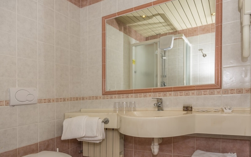 Clean bathroom with white and pink tiled walls, sink, large mirror, towel rack, and visible shower area.