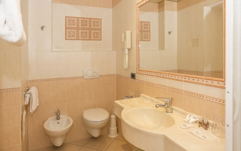 A bathroom featuring peach-patterned tiles, a sink, toilet, bidet, mirror, and towel, suggesting hotel or real estate use.