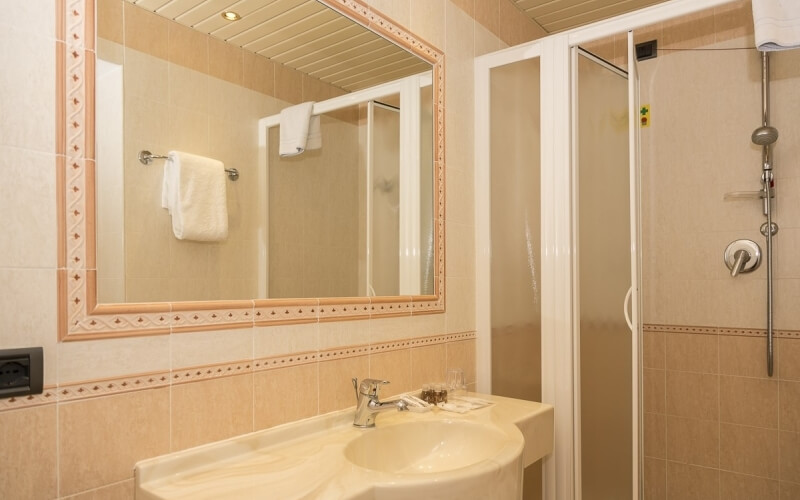 A clean bathroom with a sink, mirror, shower, beige tiles, and two glasses of amber liquid on the counter.