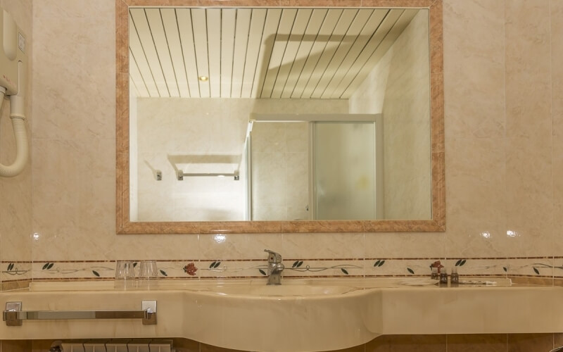 Modern bathroom with a large mirror, two sinks, beige marble countertop, and decorative items in front.