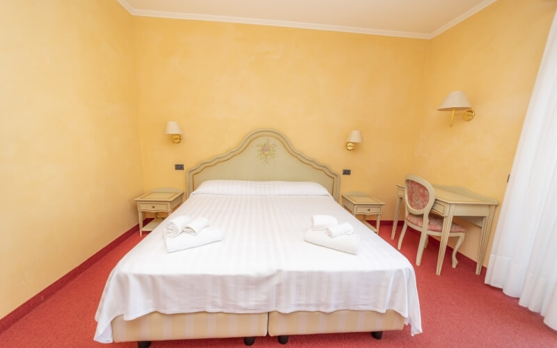 Cozy yellow bedroom with a double bed, nightstands, desk, chair, and red carpet, featuring white bedding and pink upholstery.