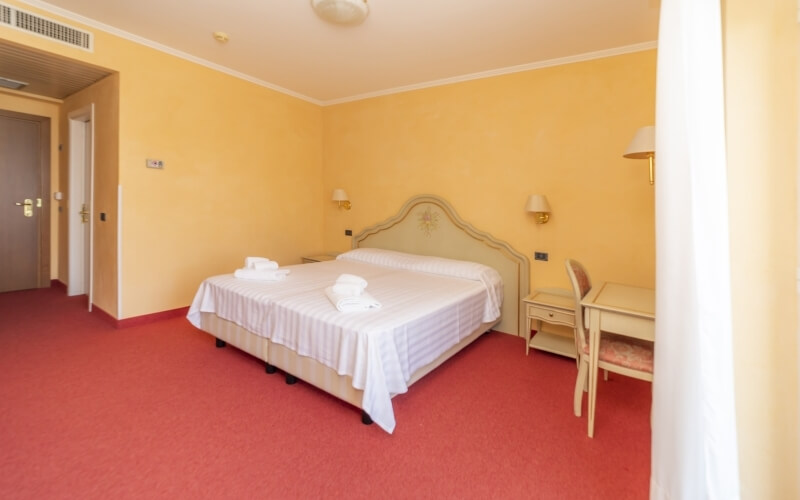 Cozy hotel room with a bed, nightstand, desk, yellow walls, red carpet, and elegant decor, creating a warm atmosphere.