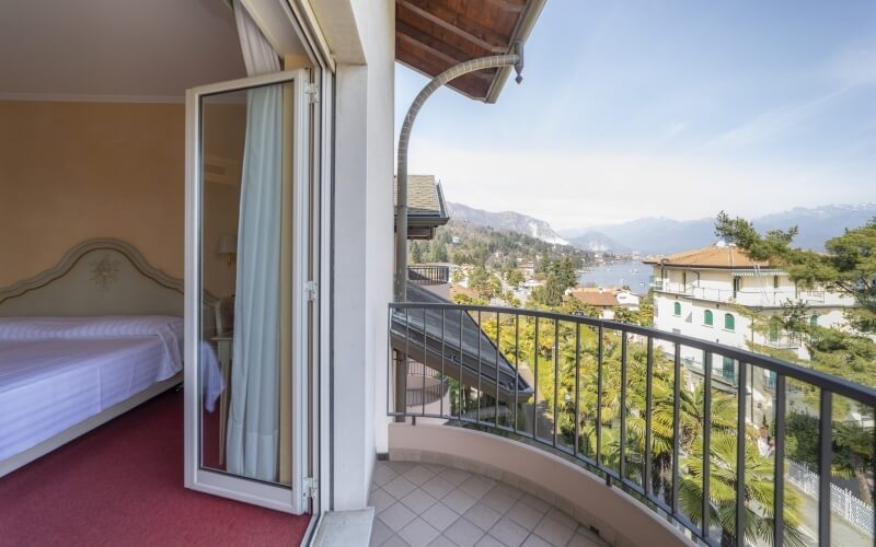 Serene bedroom with balcony view of mountains, greenery, and water, featuring a white bed and neutral decor.