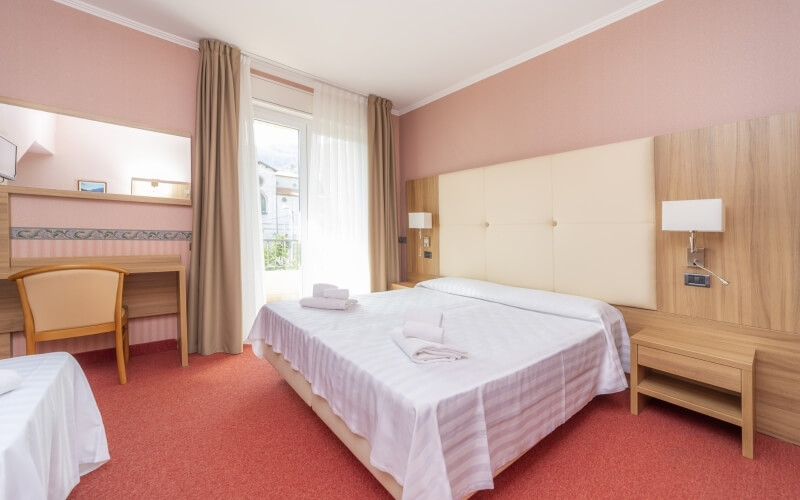 Serene hotel room with pink walls, double bed, wooden desk, large window, and elegant curtains, suggesting comfort and tranquility.