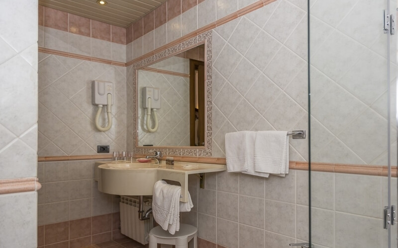 A clean bathroom with pink and white tiles, a round sink, mirror, towels, hair dryers, and a wooden ceiling.