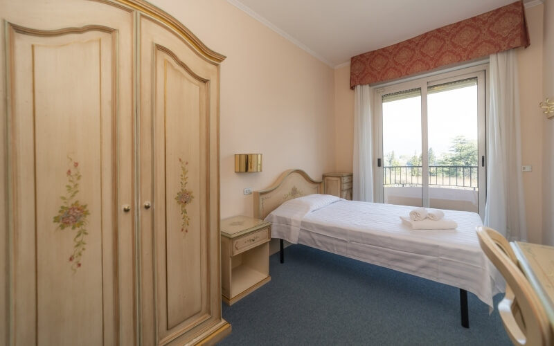 A well-lit bedroom with a bed, wardrobe, nightstand, and balcony, featuring a serene atmosphere and natural light.