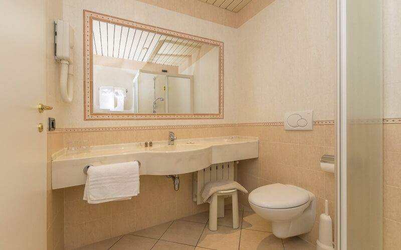 A well-lit bathroom featuring a sink, toilet, mirror, towel rack, and tile floor with white walls.