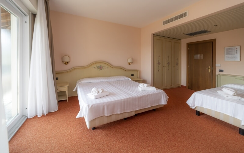 Hotel room with two beds, peach decor, white linens, wardrobe, and a door, creating a cozy and inviting atmosphere.