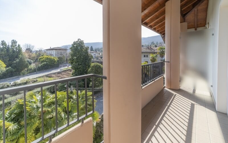 Serene balcony with vertical railing, elegant tiled floor, and a tranquil landscape of trees and houses under a clear sky.