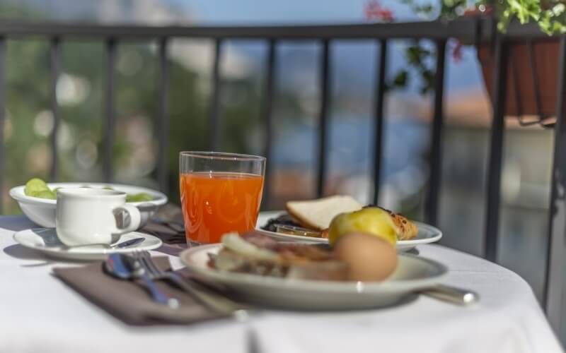 Breakfast table set with a white tablecloth, coffee cup, fruit, and scenic outdoor view with greenery in the background.