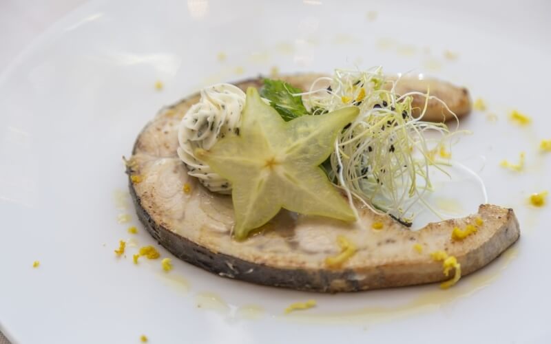 A white plate holds a cooked mushroom cap topped with starfruit and sprouts, highlighting vibrant colors and textures.