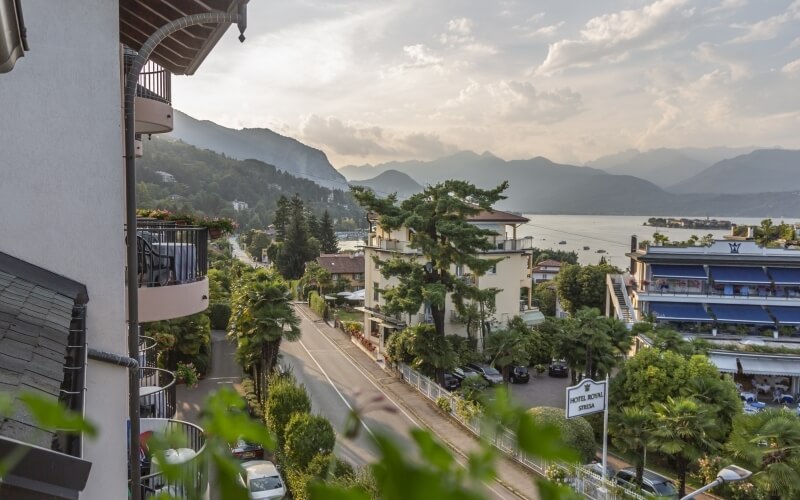 A tranquil village by a calm lake, featuring "HOTEL ROYAL," trees, parked cars, and misty mountains in the background.