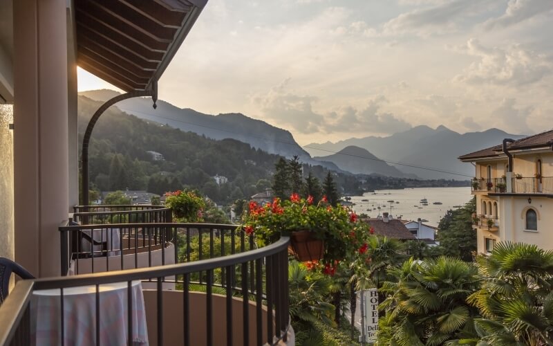 A serene balcony with a table and red flowers overlooks a misty mountain, water, and boats under an overcast sky.