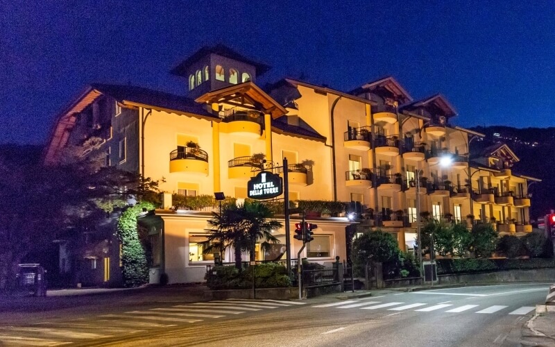 Illuminated multi-story hotel building with balconies, "HOTEL BELLA TEVERE" sign, surrounded by trees, at night.