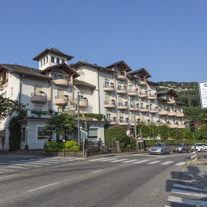Large white hotel with gray roof, balconies, and tower, at an intersection with a sign, cars, and a clear blue sky.