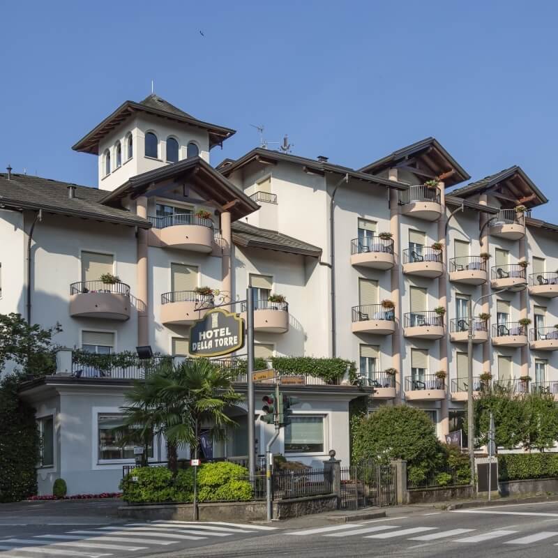 Multi-story Hotel Della Torre with a white exterior, balconies, and a tower, located near a crosswalk.