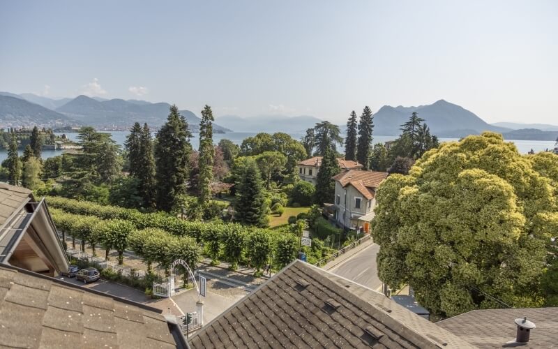 Scenic landscape with rooftops, trees, a lake, and mountains under a clear blue sky, evoking tranquility and relaxation.