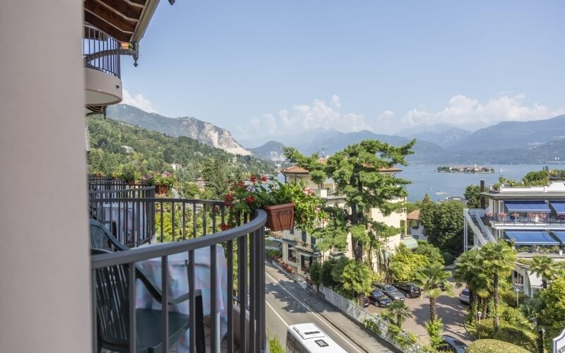 Scenic balcony view of a bustling street, serene lake, and misty mountains, adorned with plants and leisure furniture.