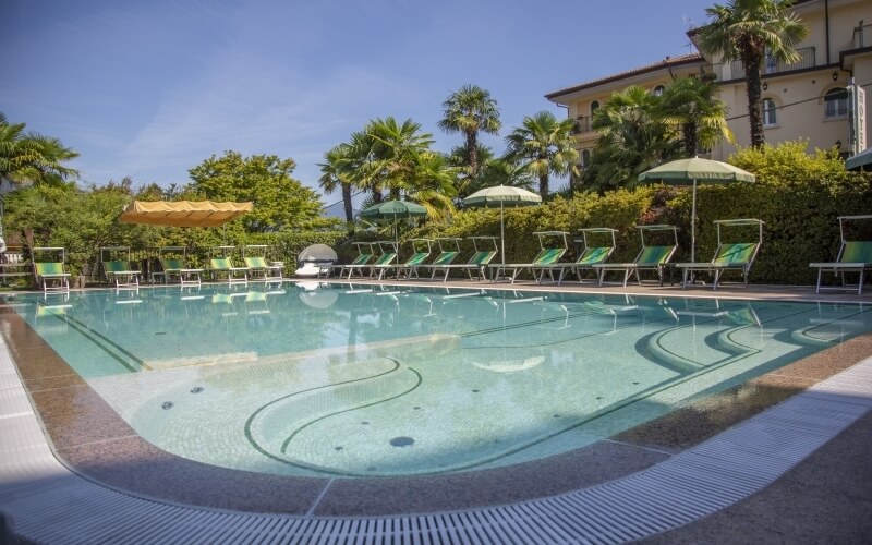 Serene pool scene with lush greenery, lounge chairs, umbrellas, and a clear blue sky, evoking tranquility and relaxation.