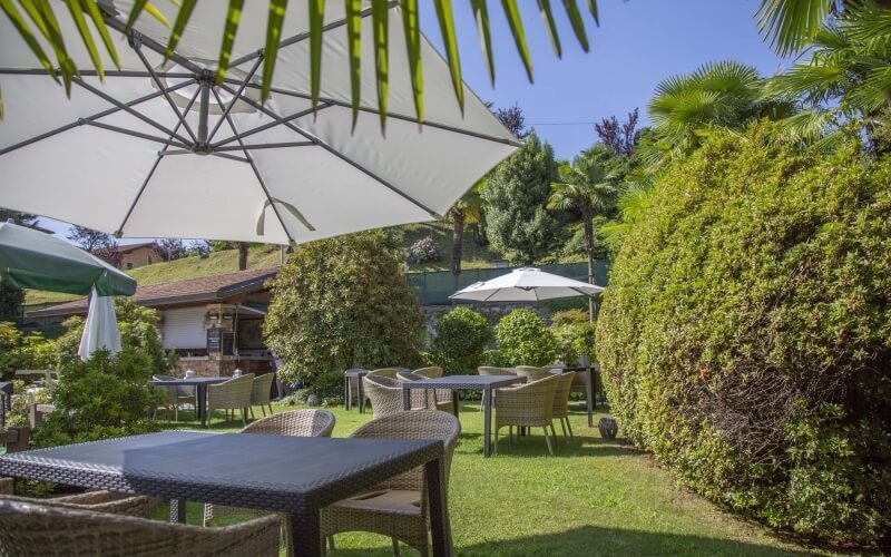 Serene outdoor seating area with tables, chairs, and umbrellas, surrounded by lush greenery under a clear blue sky.