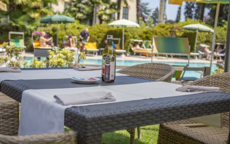 Outdoor dining setup with a wine bottle, pool area, lounge chairs, and people enjoying a sunny, tranquil day.